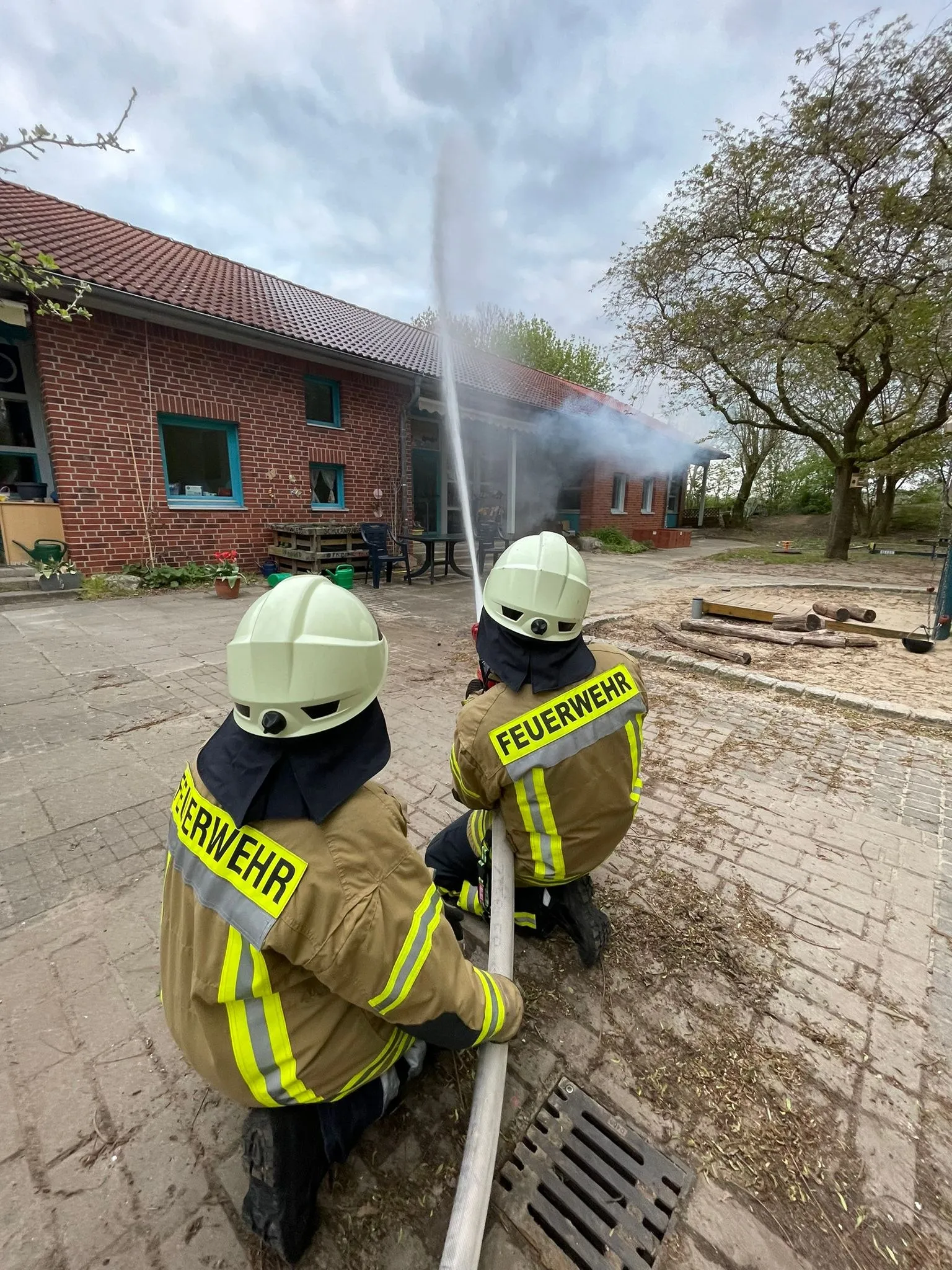 Zwei Feuerwehrleute knien mit einem Strahlrohr vor einem Gebäude